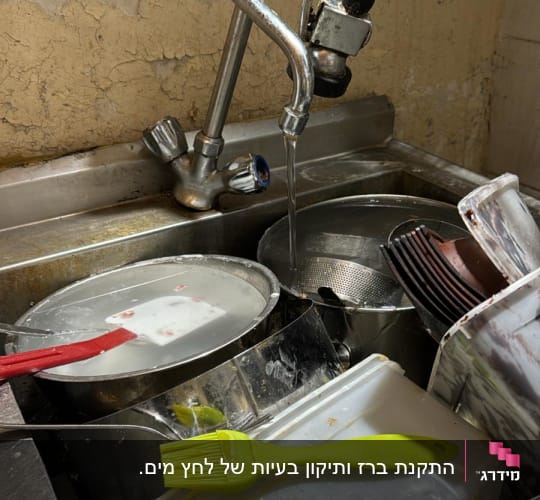 ברז מטבח עם מים זורמים בכיור מלא כלים